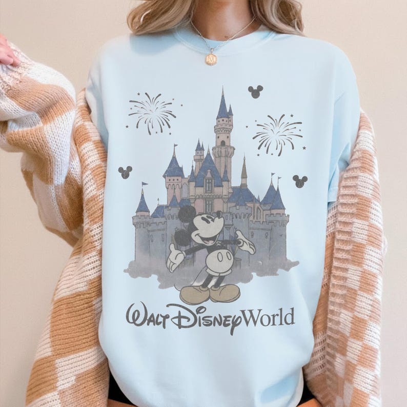 Puede incluir: Sudadera azul claro con un gr&aacute;fico de Mickey Mouse frente al castillo de Cenicienta en Walt Disney World. El dise&ntilde;o incluye fuegos artificiales y siluetas de Mickey Mouse. El texto "Walt Disney World" est&aacute; impreso debajo.