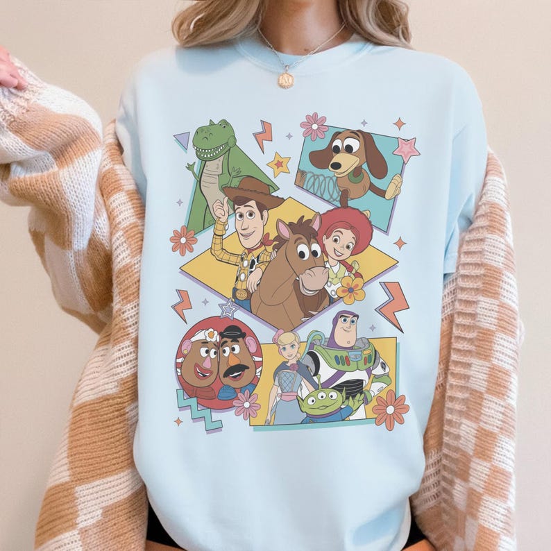 Pode incluir: Camisola azul clara com um gr&aacute;fico colorido de personagens do filme Toy Story. O design inclui Woody, Buzz Lightyear, Rex, Jessie e outros personagens, com detalhes florais e geom&eacute;tricos.