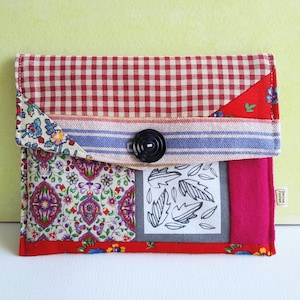 May include: A red and white gingham fabric envelope clutch with a floral print, a black button, and a black and white leaf design. The clutch has a blue and white striped fabric flap.