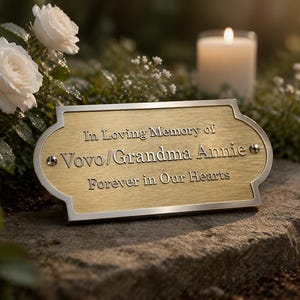 Peut inclure: Une plaque commémorative rectangulaire en métal doré brossé avec une bordure argentée et des coins décoratifs crantés. Le texte gravé indique : In Loving Memory of Vovo/Grandma Annie, Forever in Our Hearts. Fixée par deux vis argentées.