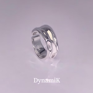 Könnte beinhalten: Ein silberner Ring mit einem einzigartigen, abstrakten Design. Der Ring ist aus glattem, poliertem Metall gefertigt und hat eine leicht strukturierte Oberfläche. Der Ring ist innen mit der Nummer "925" gekennzeichnet.