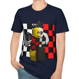 May include: Navy blue t-shirt featuring a graphic of a block figure with a crown, eye patch, and holding a box. The figure is set against a red, black, and white checkered background. The text on the box reads "BUILD TOOLS FIX".