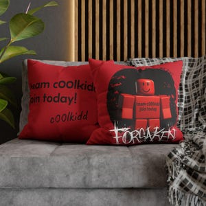 Puede incluir: Dos cojines rojos con texto y gráficos negros. Un cojín dice "team coolkidd join today! coolkidd". El otro presenta una figura de bloque roja con el texto "team coolkidd join today" y la palabra "FORGAKEN".