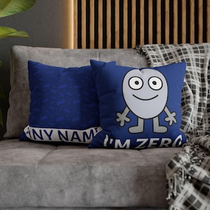 May include: Two blue throw pillows with cartoon character designs. One pillow features a smiling gray character with the text "I'M ZERO". The other pillow has a repeating pattern of the letters "bfdi" and the text "ANY NAME".