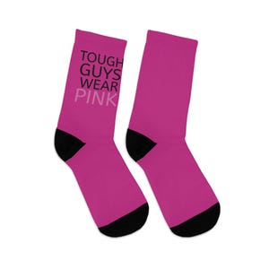 Könnte beinhalten: Ein Paar rosa Socken mit schwarzem Text, der "TOUGH GUYS WEAR PINK" lautet.