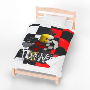 May include: A white blanket with a black, red, and white checkered pattern. The blanket features a cartoon character with a yellow head, a black eye patch, and a crown. The word "FORSAKE" is printed on the blanket.