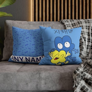 Puede incluir: Dos cojines azules sobre un sofá gris. Un cojín tiene un patrón repetido de la palabra "bfdi" en una fuente azul claro. El otro cojín tiene un diseño de personaje de dibujos animados con el texto "XFOHV!"