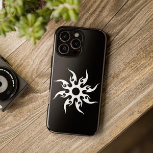 May include: Black phone case with a white tribal sun design. The phone case has a camera lens cutout and a black background.