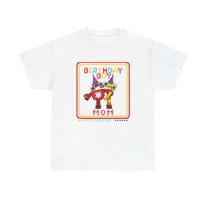 May include: White t-shirt featuring a colorful graphic of two robot-like figures with the text "BIRTHDAY BOY MOM" in a pixelated font. The design includes stars and the words "LEVEL UP".