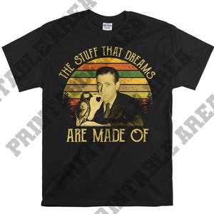 Puede incluir: Camiseta negra con un gráfico de estilo vintage que presenta a un hombre con bigote y una cita que dice "The stuff that dreams are made of."