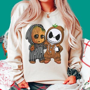 May include: A beige crewneck sweatshirt featuring a graphic print of two cartoon characters wearing each other's outfits. One character is a tree-like figure in a pinstriped suit, and the other is a skeletal figure in a brown hooded onesie.