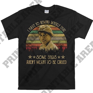 Pode incluir: Camiseta preta com um gráfico de estilo vintage de um homem com uma citação que diz "Eu tenho que me lembrar que alguns pássaros não são feitos para serem enjaulados."