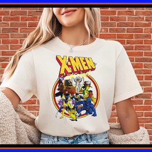 May include: A cream-coloured short-sleeve t-shirt featuring a graphic print of the X-Men logo in yellow and red text above a circular illustration of various X-Men characters including Wolverine, Beast, and Storm in their classic comic book costumes.