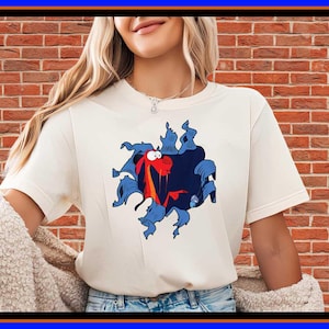 Może przedstawiać: Kremowy t-shirt z krótkim rękawem z nadrukiem graficznym przedstawiającym czerwonego smoka wyłaniającego się z ciemnoniebieskiej, poszarpanej dziury. Wzór znajduje się na środku klatki piersiowej koszulki, noszonej z beżowym kardiganem o wyraźnej fakturze.
