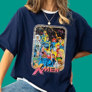 May include: A navy blue short-sleeve t-shirt featuring a rectangular graphic print of the X-Men comic book characters in a space setting. The design includes a colourful group of superheroes and the bold pink and yellow X-MEN logo at the bottom.