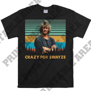 Op de afbeelding: Zwart T-shirt met een vintage afbeelding van Patrick Swayze uit de film 'Point Break'. De afbeelding is omgeven door een gestreepte achtergrond en de tekst 'Crazy for Swayze'.