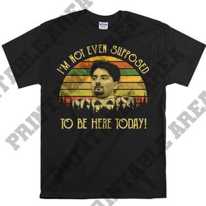 May include: Black t-shirt with a vintage-style graphic featuring a man's face and the text "I'm not even supposed to be here today!"