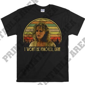 Puede incluir: Camiseta negra con una imagen retro de una mujer con cabello rubio y el texto "No me ignorarás, Dan!"