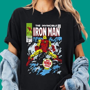 May include: A black short-sleeved t-shirt featuring a graphic print of The Invincible Iron Man comic book cover. The design includes the title, a red and yellow Iron Man character, and the text Big Premiere Issue in a circular badge.