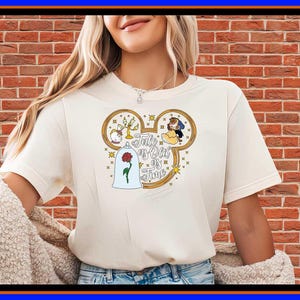 Puede incluir: Una camiseta de manga corta de color crema con un gráfico en forma de silueta de Mickey Mouse que contiene ilustraciones de personajes y una rosa bajo una cúpula de cristal, con el texto Tale as Old as Time escrito en letra cursiva.