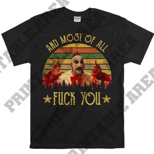 Puede incluir: Una camiseta negra con un gráfico de estilo vintage de un payaso con una nariz roja y un sombrero rojo, blanco y azul. El gráfico está sobre un fondo de puesta de sol con el texto "And most of all, F*** You" en amarillo.