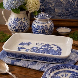 May include: A rectangular white ceramic baking dish featuring a blue willow pattern on the interior base and exterior sides. The design depicts traditional pagodas, trees, and birds in a classic blue and white color scheme on the glazed surface.