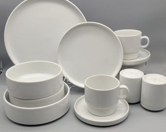 May include: A white ceramic dinnerware set, including large plates, smaller plates, bowls, cups, saucers, and salt and pepper shakers. The set has a minimalist design with a clean, modern aesthetic, perfect for everyday use or special occasions.