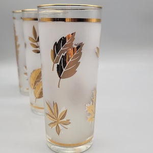 May include: Set of three frosted highball glasses with gold leaf designs. Each glass features a gold rim and is adorned with various gold and brown leaf patterns. The glasses are ideal for serving beverages.