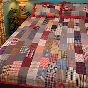 May include: A patchwork quilt and two matching pillow shams featuring a variety of rectangular fabric swatches in plaid, checkered, and striped patterns. The bedding set is finished with a solid red fabric border and ruffled red trim edges.