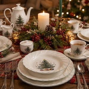 May include: A white porcelain dinnerware set featuring a green Christmas tree pattern with scalloped edges. The collection includes plates, bowls, cups, saucers, a teapot, a creamer, and a sugar bowl, all arranged on a red and green plaid tablecloth.