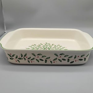 May include: Rectangular off-white ceramic baking dish with a green holly and berry design around the edges and center. The dish has a green trim and handles on each side. A festive piece for holiday baking.