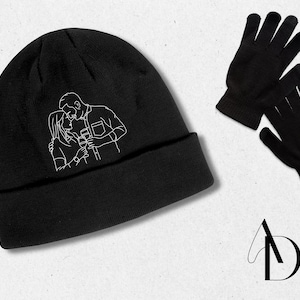 Può includere: Berretto nero con un contorno bianco di una coppia che si bacia. Il berretto è realizzato in un materiale morbido e confortevole e ha un risvolto.