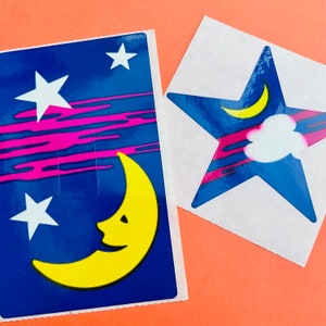 Könnte beinhalten: Zwei Aufkleber mit Nachthimmel-Motiv. Ein Aufkleber zeigt einen Halbmond mit einem lächelnden Gesicht und Sternen. Der andere Aufkleber zeigt einen blauen Stern mit rosa und weißen Streifen und einer Wolke.