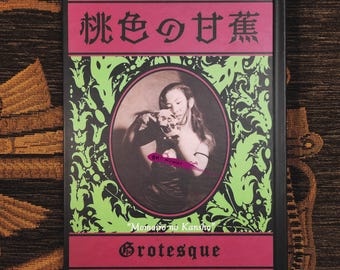 May include: A hardback book with a black cover featuring a central oval portrait of a person holding a skull. The design includes bright green ornate patterns, pink horizontal bands, and the text 桃色の甘蕉, Oh! Kowai, Momoiro no Kansho, and Grotesque.