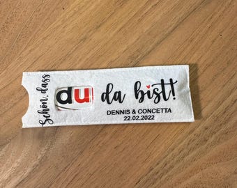 Puede incluir: Una funda de fieltro blanco con el texto "Schön, dass du da bist!" y los nombres "DENNIS & CONCETTA" con la fecha "22.02.2022". La funda contiene un producto Nutella.
