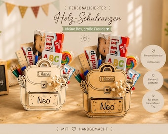 Puede incluir: Dos cajas de madera con forma de mochila escolar llenas de útiles escolares, caramelos y una pequeña caja de chocolate. Las cajas están personalizadas con el nombre "Neo" y el texto "1. Klasse". El texto "Mein erster Schultag" está en una pequeña pizarra.