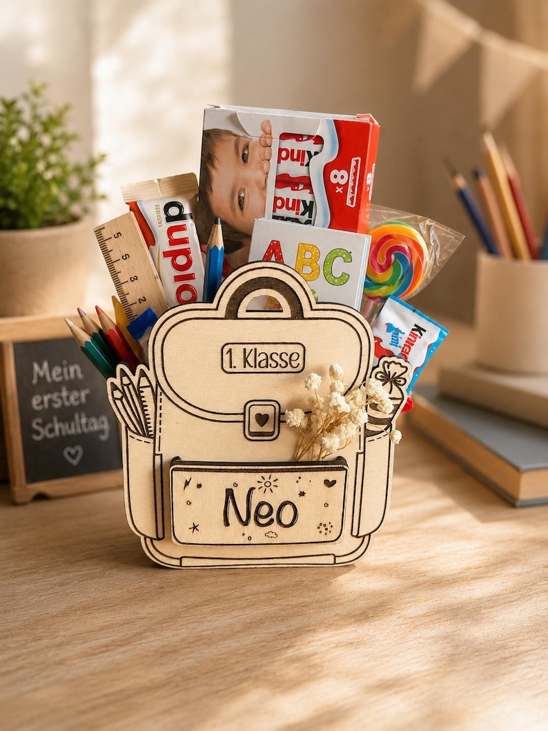 Puede incluir: Un organizador de escritorio de madera con forma de mochila, lleno de &uacute;tiles escolares y golosinas. El organizador tiene el nombre "Neo" en la parte delantera y las palabras "1. Klasse" en la parte superior. Contenido: l&aacute;pices, una regla, caramelos y una caja Kinder Sorpresa.
