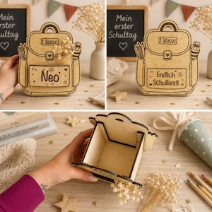 Puede incluir: Caja de madera con forma de mochila con el nombre "Neo" grabado en la parte delantera. La caja est&aacute; llena de flores secas y tiene un peque&ntilde;o compartimento en el interior. Las palabras "1. Klasse" tambi&eacute;n est&aacute;n grabadas.