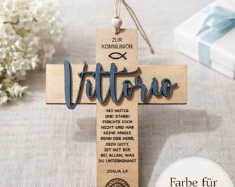 Puede incluir: Cruz de madera con el nombre "Vittorio" en escritura azul. La cruz incluye texto en alemán y una pequeña etiqueta de madera que dice "Zur Kommunion" con un símbolo de pez. Un arcoíris está en la parte inferior.