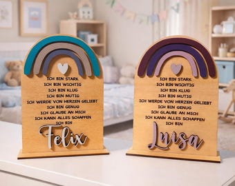 Puede incluir: Dos placas de madera en forma de arcoíris, con los nombres "Felix" y "Luisa". Cada placa presenta un diseño de arcoíris en tonos de azul, gris y marrón, o morado, rosa y marrón. El texto de las placas está en alemán.