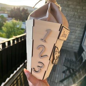 Puede incluir: Un recipiente de madera en forma de cono con los n&uacute;meros 1, 2 y 3 adjuntos. Una peque&ntilde;a etiqueta de madera con el nombre "Jones" est&aacute; en el lateral. La parte superior est&aacute; cubierta con una tela beige atada con hilo. Un art&iacute;culo decorativo.