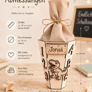 Puede incluir: Caja de regalo c&oacute;nica de madera personalizada, de aproximadamente 20 cm de alto y 14 cm de di&aacute;metro, con un dise&ntilde;o de dinosaurio y el nombre "Jonas". La caja est&aacute; rellena con una bolsa de tela beige atada con hilo. El texto "Endlich Schulkind" es visible.