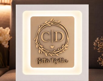 Puede incluir: Una pieza de arte mural iluminada y enmarcada en blanco. La obra presenta un panel rectangular dorado con un diseño circular de las letras "CD" dentro de una corona, un corazón y las palabras "Better together".