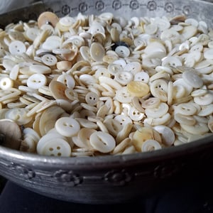 May include: A bowl filled with a large collection of white and cream colored buttons of various sizes and shapes.