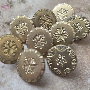 May include: A collection of antique brass buttons with intricate floral and geometric designs. The buttons are round, with detailed embossed patterns and a warm, golden hue. These vintage buttons are ideal for sewing and craft projects.