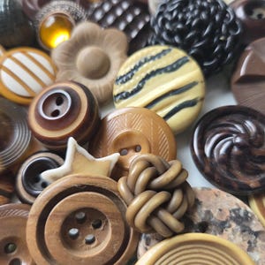 May include: A collection of vintage buttons in various shapes, sizes, and colors. The buttons include a range of materials, such as wood, plastic, and possibly glass. Colors include shades of brown, tan, cream, and black. Some buttons have striped, floral, or swirl designs.