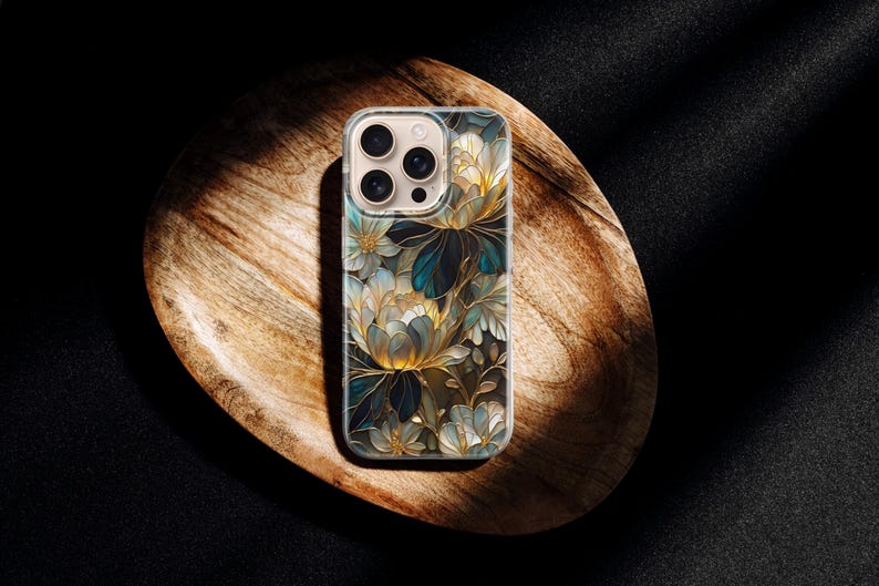 Puede incluir: Funda transparente para tel&eacute;fono con un dise&ntilde;o floral con flores azules, doradas y blancas. La funda est&aacute; sobre una bandeja de madera con un fondo oscuro. El estampado floral tiene un aspecto art&iacute;stico detallado.