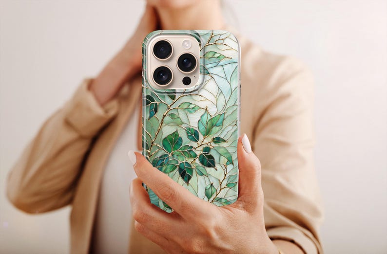 Puede incluir: Funda de tel&eacute;fono inteligente con un dise&ntilde;o bot&aacute;nico. La funda presenta hojas verdes y vetas doradas sobre un fondo azul claro. La funda tiene un acabado brillante y un parachoques protector. La funda del tel&eacute;fono est&aacute; en la mano de una persona.