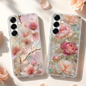 May include: Two clear phone cases with floral designs. One case features pink and white flowers with gold accents, while the other showcases pink and cream peonies. The cases have a glossy finish and a three-lens camera cutout.