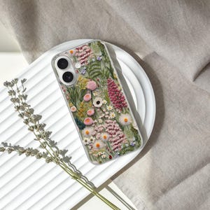 May include: A clear phone case with a floral design featuring pink, white, and green flowers. The case is designed to fit a smartphone.
